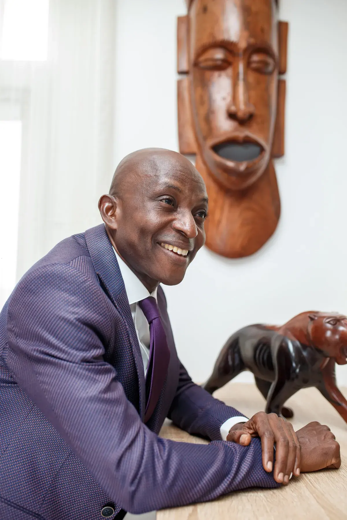 Richard Meseko smiling beside a carved wooden mask.