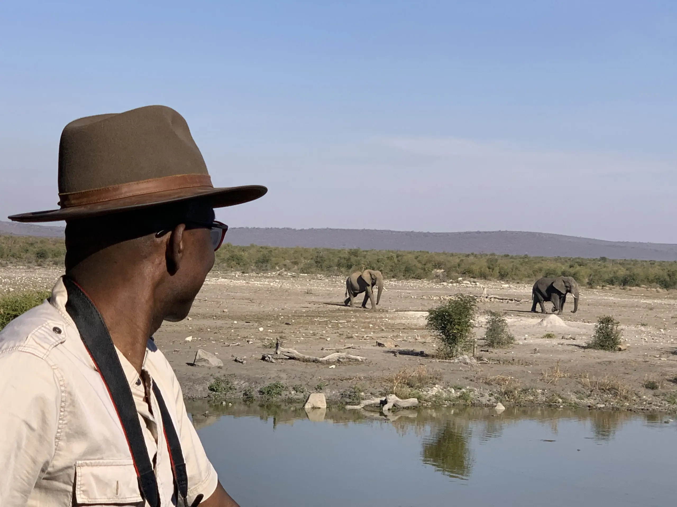 Richard Meseko in a hat watching elephants across a river.